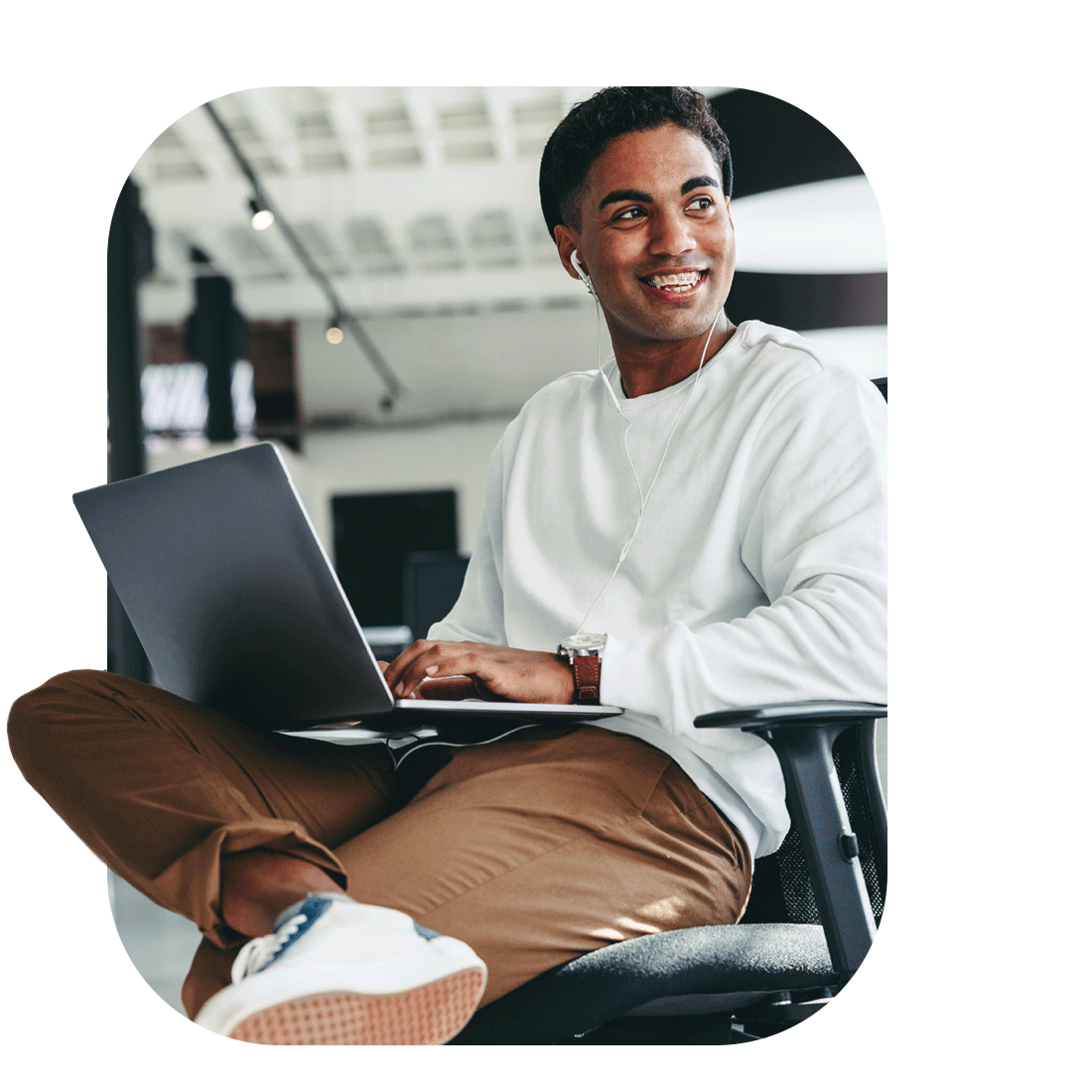 A man comfortably sitting on a chair, working on a laptop in a bright and organized office setting.