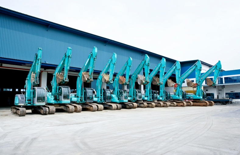 A group of blue excavators parked in front of a building, showcasing construction equipment ready for work.