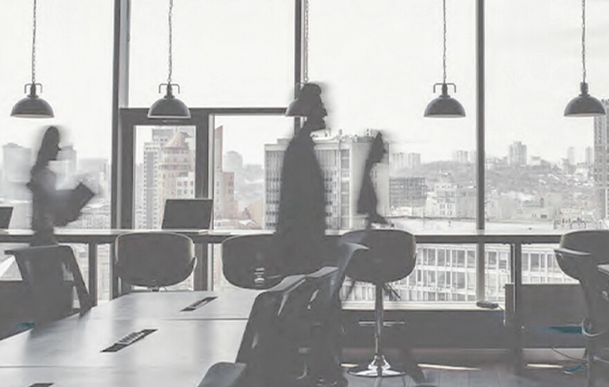 Academic research office with large windows facing city skyline with blurred figures walking between desks and pendant lights
