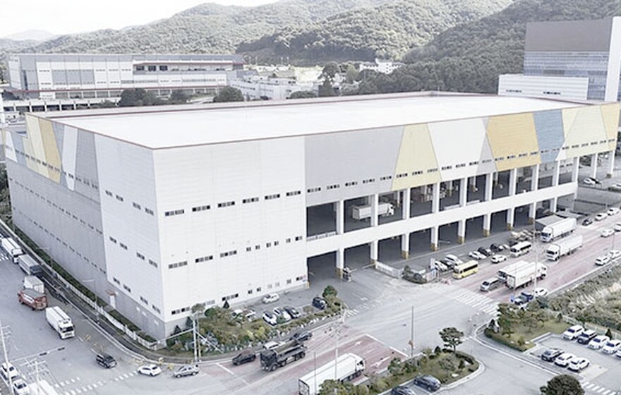 Aerial view of a massive white warehouse with colorful geometric accents and a busy loading dock with several trucks.
