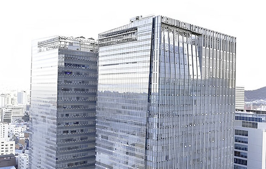 Two modern glass skyscrapers with reflective blue windows stand tall against a bright city skyline background.