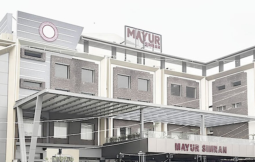 Modern multi-story hotel building with brick and white facade featuring a large MAYUR SIMRAN sign on the roof.
