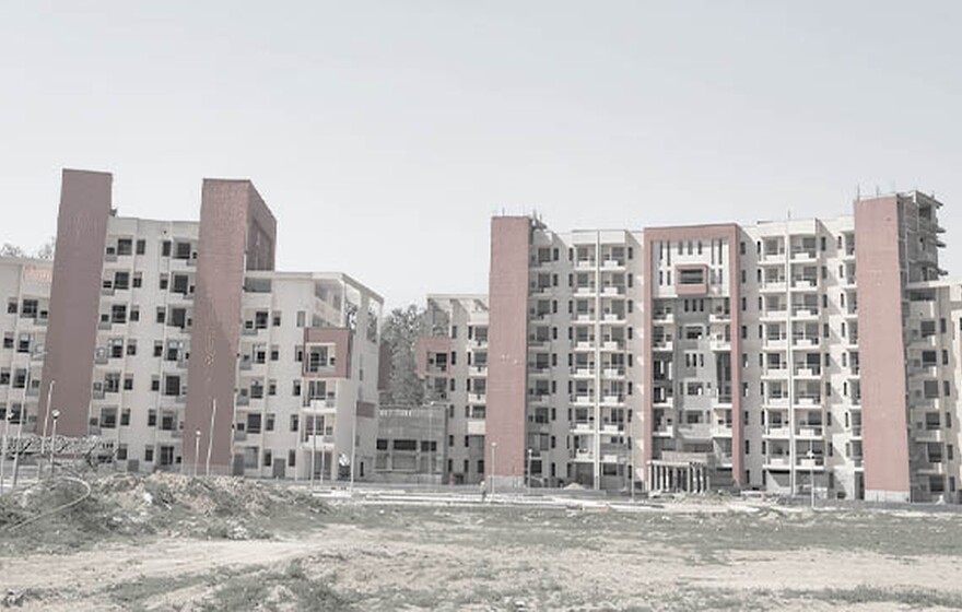 Two large, multi-story dormitory buildings under construction with beige facades and prominent vertical red brick sections.