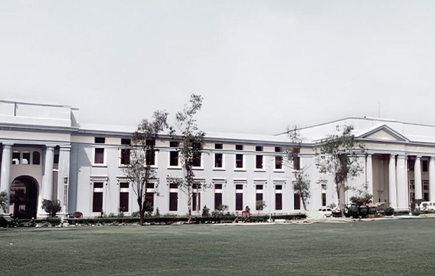 Elegant neoclassical building with large columns, pale blue facade, surrounded by green lawns and trees, exuding grandeur and calm.