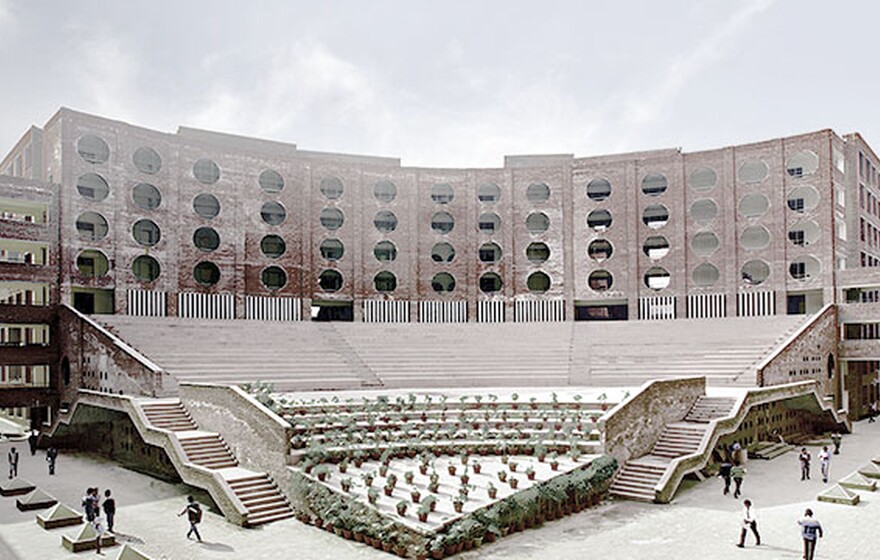 Modern red-brick university building with circular windows, large open amphitheater steps, landscaped courtyard, and students walking around.