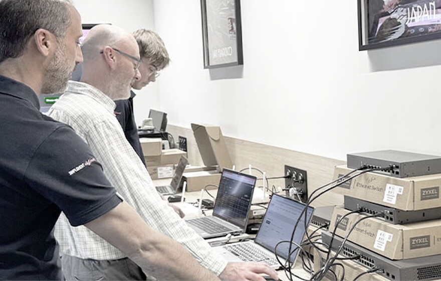 Nebula MSP Pack case study. IT staff configure Zyxel Ethernet switches and laptops in a workspace with monitoring screens.