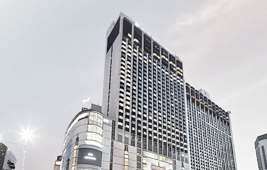 Exterior view of a modern five-star hotel in Myeongdong, Seoul, with illuminated windows and skyline at dusk.