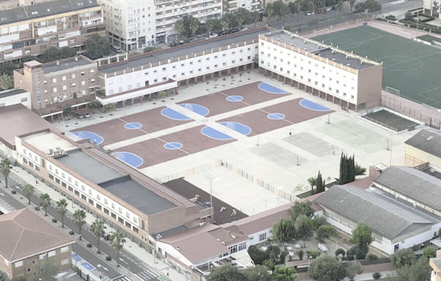 An aerial view of a school campus with buildings, basketball courts, and a soccer field in a residential area.