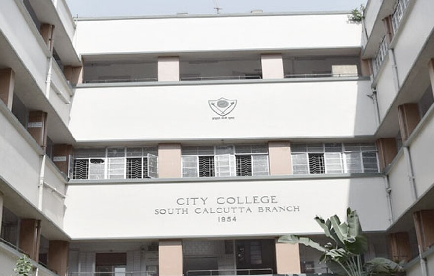 Front view of City College South Calcutta Branch building, showing a three-floor structure surrounded by greenery and flowering plants.