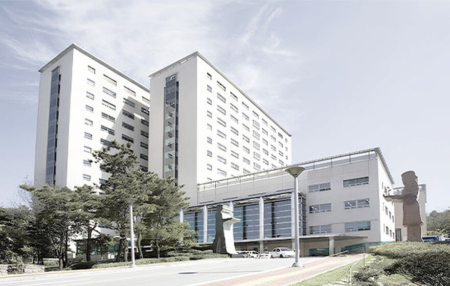 Large modern white university building with multiple wings and glass entrances under a bright blue sky in South Korea.