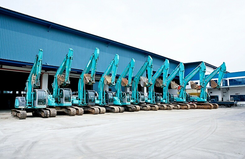 A group of blue excavators parked in front of a building, showcasing construction equipment ready for work.