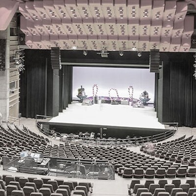 Spacious modern concert hall with red ceiling panels, tiered seating, wooden acoustic design, and a brightly lit stage prepared for performance.