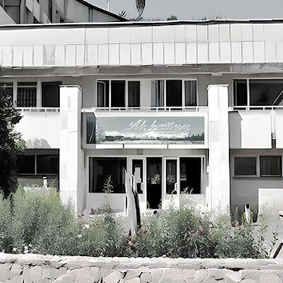 Front view of Ak-Kayyn Sanatorium with stone walls, green benches, and a garden, showing its unique 1970s architecture under clear blue sky.