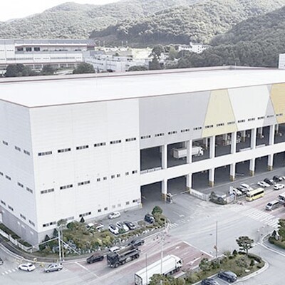 Aerial view of a massive white warehouse with colorful geometric accents and a busy loading dock with several trucks.