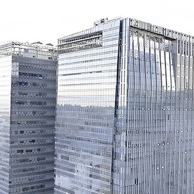 Two modern glass skyscrapers with reflective blue windows stand tall against a bright city skyline background.