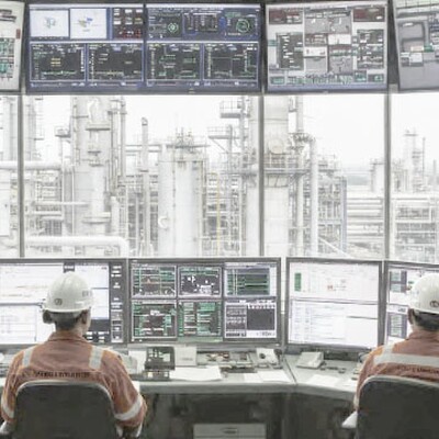 Two operators in a control room monitor industrial plant data on a massive video wall and multiple desktop display screens.