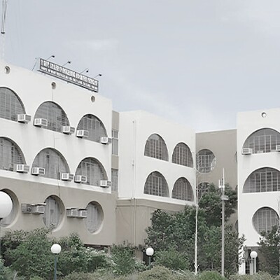 One Indian school building with arched and circular windows, yellow and white facade, lush greenery, and clear blue sky.