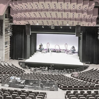 Spacious modern concert hall with red ceiling panels, tiered seating, wooden acoustic design, and a brightly lit stage prepared for performance.