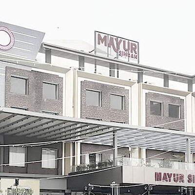 Modern multi-story hotel building with brick and white facade featuring a large MAYUR SIMRAN sign on the roof.