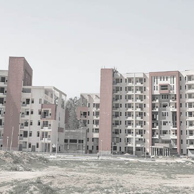 Two large, multi-story dormitory buildings under construction with beige facades and prominent vertical red brick sections.