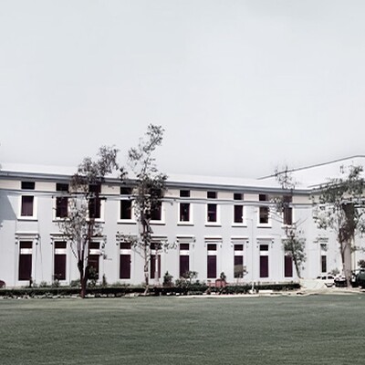 Elegant neoclassical building with large columns, pale blue facade, surrounded by green lawns and trees, exuding grandeur and calm.