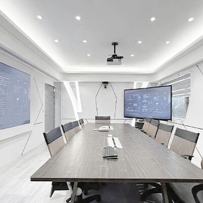 Modern conference room with a long wood table, orange chairs, and dual blue digital screens showing technical AV diagrams.