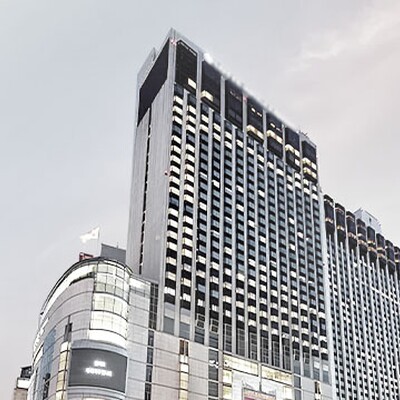 Exterior view of a modern five-star hotel in Myeongdong, Seoul, with illuminated windows and skyline at dusk.