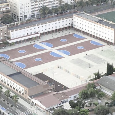 An aerial view of a school campus with buildings, basketball courts, and a soccer field in a residential area.