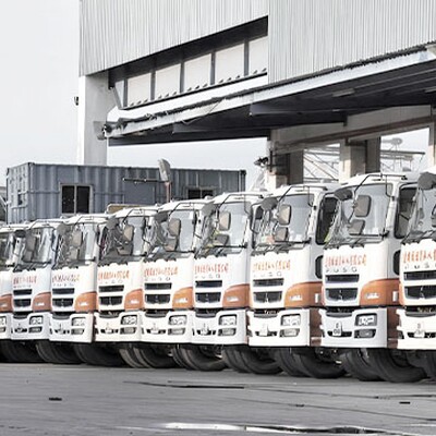 A row of trucks was parked neatly outside a large industrial warehouse under a clear sky, ready for transportation or delivery.