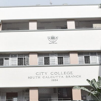 Front view of City College South Calcutta Branch building, showing a three-floor structure surrounded by greenery and flowering plants.