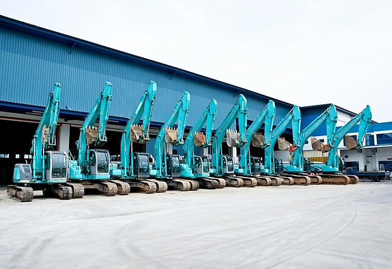 A group of blue excavators parked in front of a building, showcasing construction equipment ready for work.
