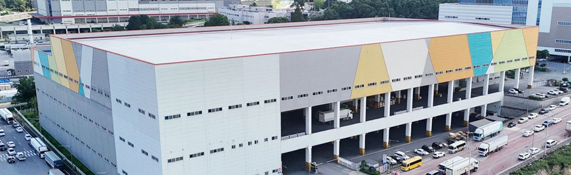 Aerial view of a massive white warehouse with colorful geometric accents and a busy loading dock with several trucks.
