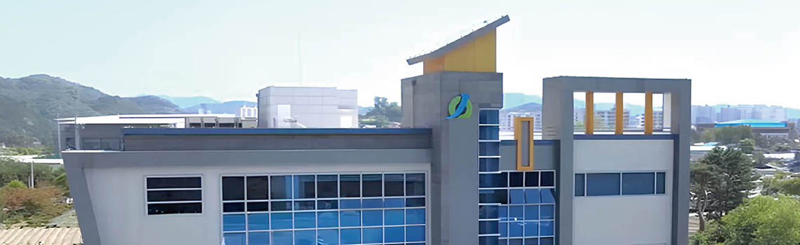 Modern fire safety training institute building with blue glass windows, a light gray facade, and a stylized green/blue logo.
