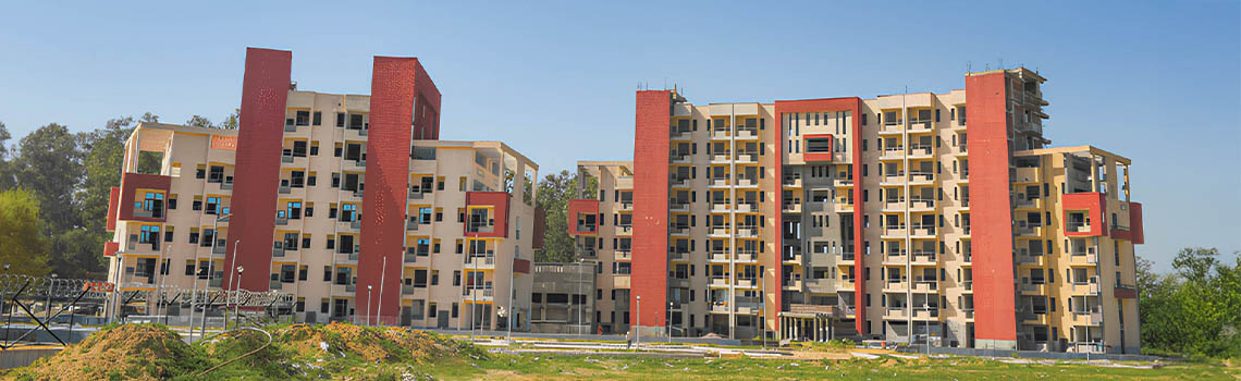 Two large, multi-story dormitory buildings under construction with beige facades and prominent vertical red brick sections.