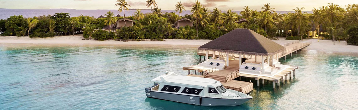 A white boat docked at a wooden pier leading to the JW Marriott Maldives Resort & Spa pavilion.