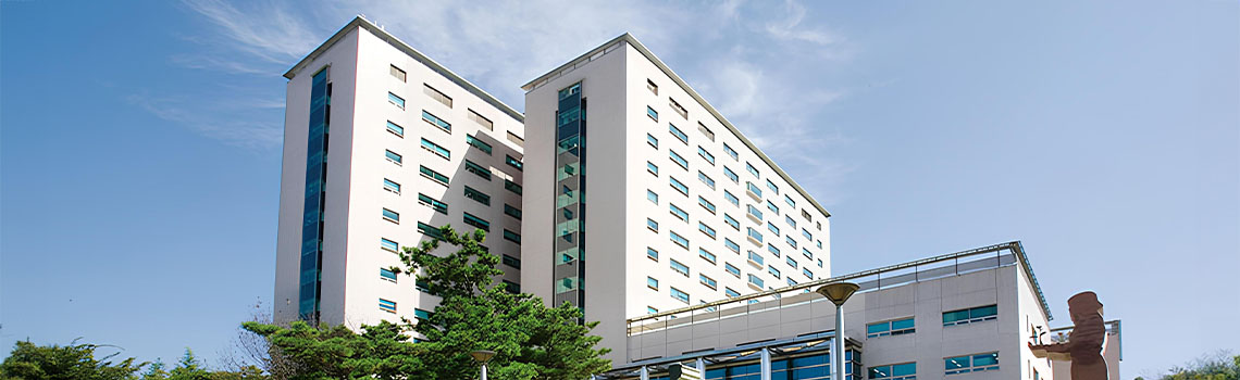 Large modern white university building with multiple wings and glass entrances under a bright blue sky in South Korea.